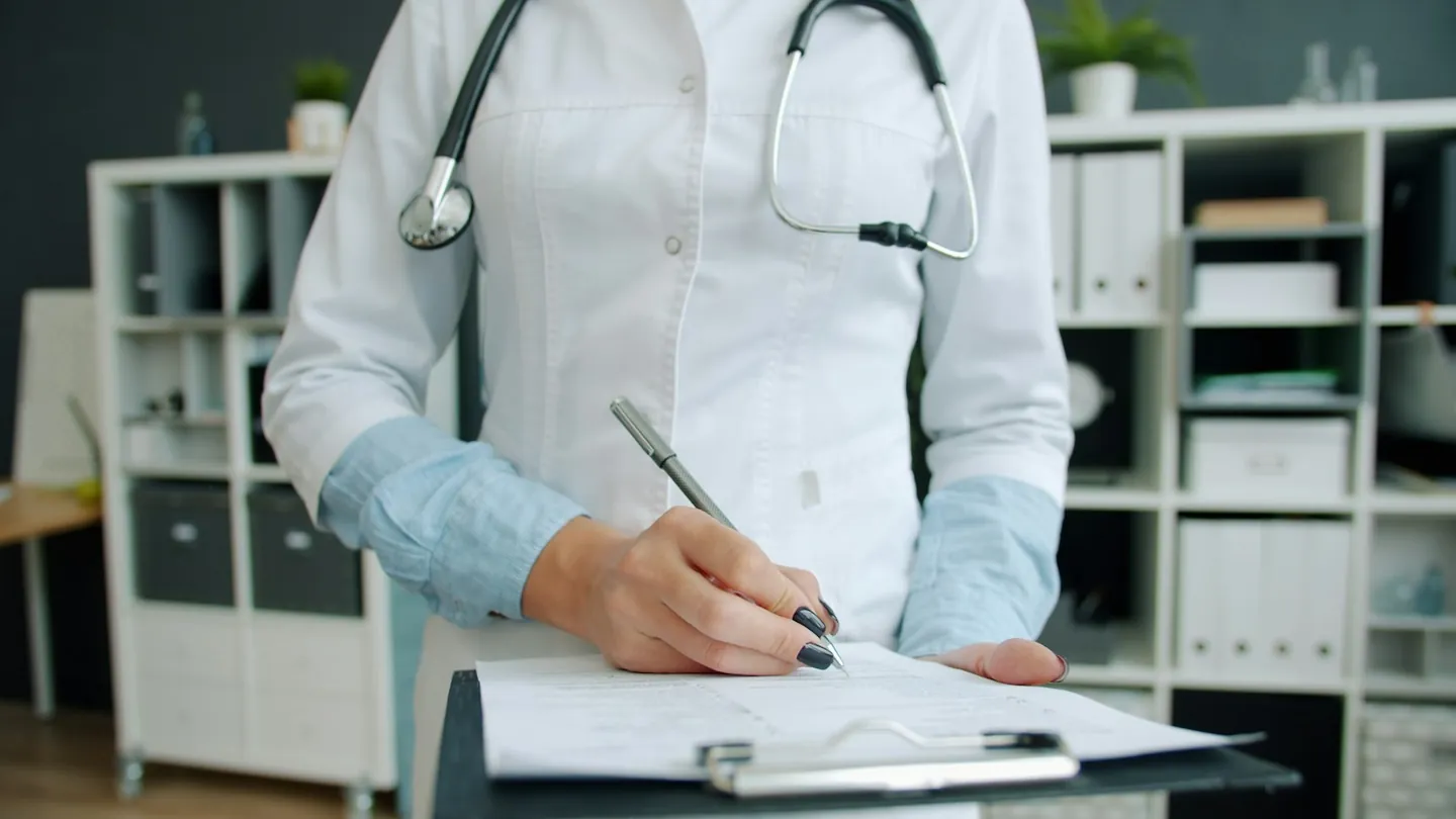 Doctor writing clinical notes on a clipboard during a supervised assessment